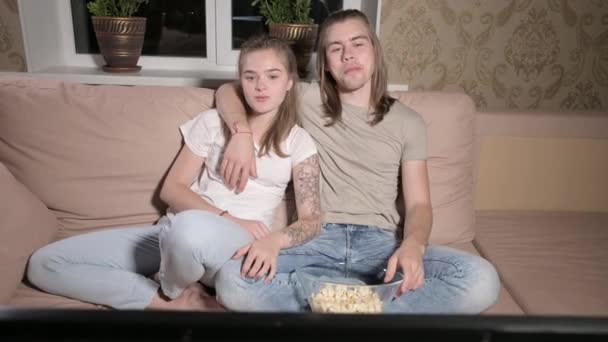 Junges nettes Paar, das sich im Wohnzimmer umarmt, fernsehen und Popcorn essen. — Stockvideo