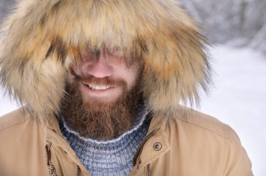Kapüşonlu bir ceket giymiş sırıtık bir adam. Kaputun altından sert bir şekilde giyinmiş. Kış ormanındaki bir insanın ciddi bir portresi. Açık hava zamanı.