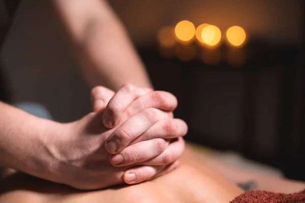 Close-up of the hands of a male masseur doing back massage to a girl at the spa. Low key high contrast shallow depth of field — Stock Photo, Image