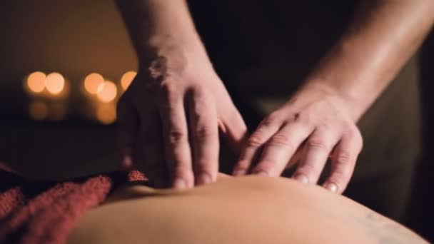 Pria muda terapi pijat sedang melakukan pijat jari seorang wanita kembali dengan tato di ruang pijat dengan lampu redup di latar belakang lilin. Konsep pijat premium tombol rendah — Stok Video