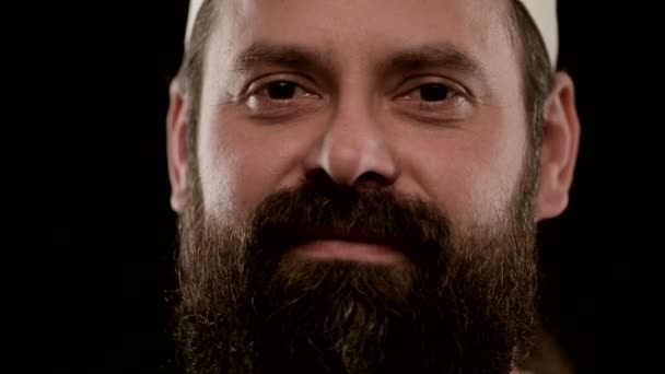 Homem com barba no estúdio em fundo preto coloca em uniforme de cozinheiro. Close-up — Vídeo de Stock