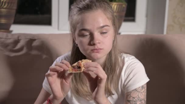 Jeune femme mignonne est assise dans le salon sur le canapé, regarde la télévision, mange de la pizza. Gros plan — Video