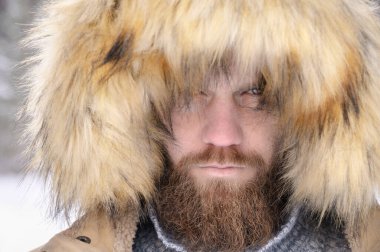 Kapüşonlu sıradan bir ceket giymiş bir adam kaputun altından kışın ormanda bir insanın ciddi bir portresini giymiş. Açık hava zamanı.