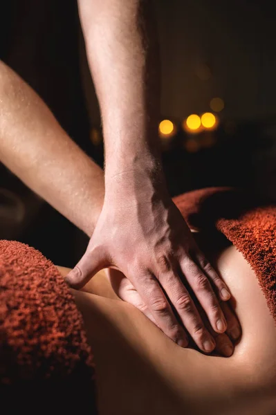 Zbliżenie dłonie Profesjonalny masaż premium w ciemnej szafie atmosferycznej. Młody mężczyzna robi masaż kobiecie klientce w ciemnym biurze na tle palących się świec — Zdjęcie stockowe