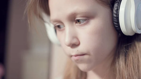 Zbliżenie ujęcia portretu popędliwego planu poważnej zamyślonej i oderwanej dziewczyny, która ma 10 lat w dużych białych słuchawkach w pomieszczeniu. Wygląd boczny — Zdjęcie stockowe