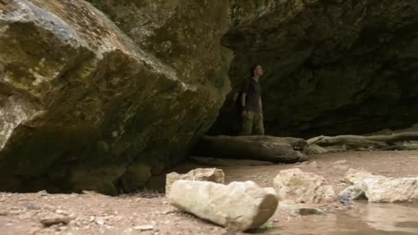 Joven con mochila sube a la piedra mirando la hermosa vista de la cascada — Vídeos de Stock