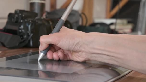Närbild av en manlig designer drar på sin bärbara dator med hjälp. grafisk tablett och penna stylus Mot bakgrund av sin Slr kamera — Stockvideo