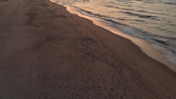 Під час заходу сонця над безлюдним пляжем літають безпілотні літаки. Піщаний берег з хвилями, що котилися, і сонце, що сідає за обрій. Морська плита — стокове відео