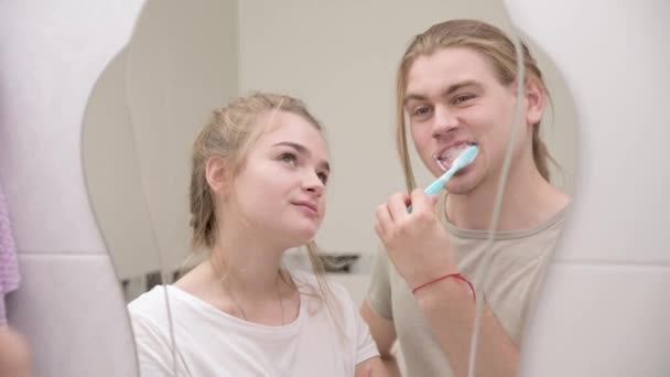 Pareja en el baño, mirando el reflejo en el espejo. El hombre cepilla los dientes. Primer plano — Vídeos de Stock