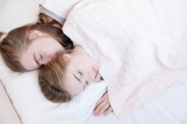 Yatakta genç bir çiftin, bir battaniyenin arkasına saklanarak kucaklaşarak uyuduğu yakın plan. Genç aile kavramı ve sağlıklı uyku.