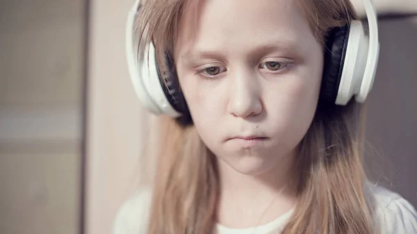 Zbliżenie ujęcia portretu popędliwego planu poważnej zamyślonej i oderwanej dziewczyny, która ma 10 lat w dużych białych słuchawkach w pomieszczeniu. Wygląd boczny — Zdjęcie stockowe