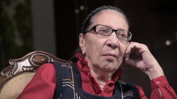 Retrato de una anciana pensativa con gafas apoyadas en su brazo, sentada y pensando. Mujer mayor 80 años — Vídeo de stock