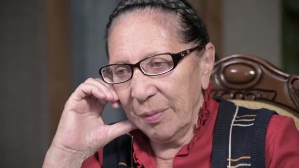 Portrait d'une femme âgée et chérissante portant des lunettes, appuyée sur son bras à l'intérieur, assise et réfléchie. Femme âgée 80 ans — Video