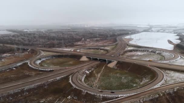 Luftaufnahmen von Autos und Lastwagen, die sich an einer winterlichen Kreuzung bewegen, sind eine große Straßenkreuzung. unbemannter Blick auf den Autoverkehr auf einer Autobahn in den Vororten im Winter. Kreisverkehr an der Kreuzung — Stockvideo