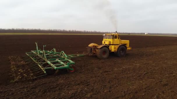 Повітряний вигляд потужного жовтого трактора з великими зусиллями на гачку, що виконує оранку грунт для посіву зимових культур з дисковим культиватором восени — стокове відео