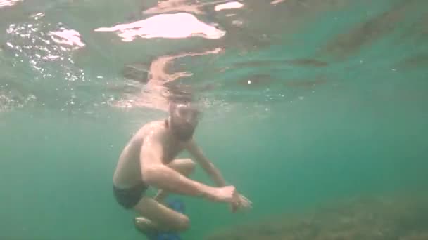 Un hombre delgado con barba en una máscara nada bajo el agua, agitando los brazos. Primer plano . — Vídeos de Stock