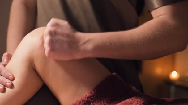 Close-up van een professionele masseur man laat een klant de benen en knieën masseren in een kantoor met schemerige verlichting tegen de achtergrond van brandende kaarsen. Premium massage service voor luxe klanten — Stockvideo