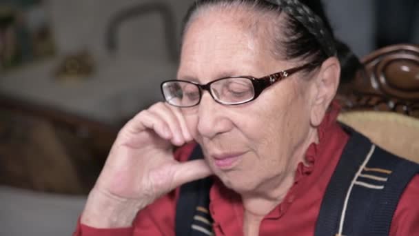 Portrait d'une femme âgée et chérissante portant des lunettes, appuyée sur son bras à l'intérieur, assise et réfléchie. Femme âgée 80 ans — Video