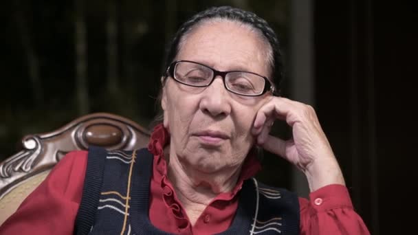 Portrait d'une femme âgée et chérissante portant des lunettes, appuyée sur son bras à l'intérieur, assise et réfléchie. Femme âgée 80 ans — Video