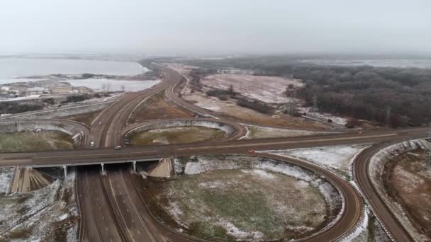 Zdjęcie lotnicze samochodów osobowych i ciężarowych poruszających się na zimowym skrzyżowaniu to duży węzeł drogowy. Bezzałogowy widok ruchu samochodowego na autostradzie na przedmieściach w zimie. Karuzela na skrzyżowaniu — Wideo stockowe