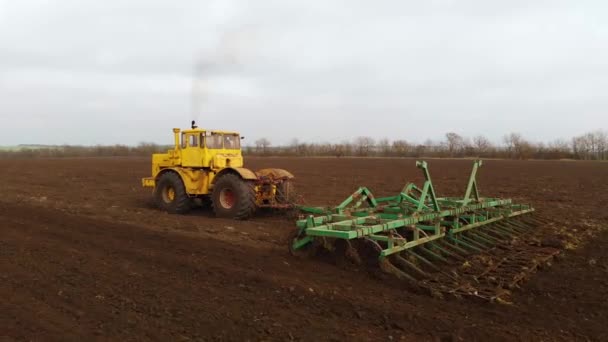 Luftaufnahme eines gelben Traktors mit Anhänger, der ein Land pflügt, bevor er Getreide anpflanzt. das Konzept der Bodenvorbereitung für die Aussaat von Saatgut im Boden. Bauernhof — Stockvideo