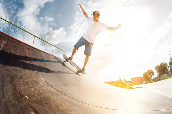 Πορτρέτο ενός νεαρού skateboarder κάνει ένα τέχνασμα για skateboard του σε μια ράμπα μισό σωλήνα σε ένα πάρκο skate το καλοκαίρι σε μια ηλιόλουστη μέρα. Η έννοια της νεανικής κουλτούρας του ελεύθερου χρόνου και του αθλητισμού — Φωτογραφία Αρχείου