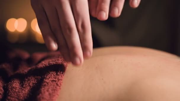 Genç erkek masaj terapisti, arka planında loş ışık olan masaj odasında dövmesi olan bir kadına parmak masajı yapıyor. Düşük tuşlu premium masaj konsepti — Stok video