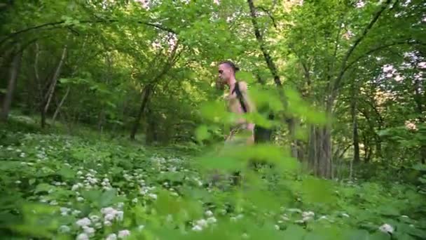 Jongeman loopt door de struiken van bloemen in het bos. Zomerdag — Stockvideo