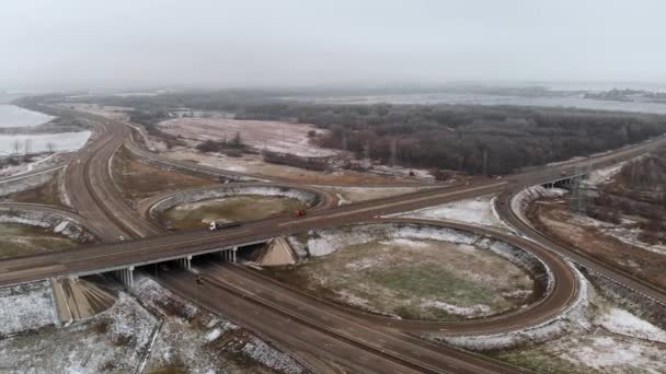 Letecký záběr osobních a nákladních automobilů pohybujících se na zimní křižovatce je velkým silničním uzlem. Bezpilotní pohled na automobilovou dopravu na dálnici na předměstí v zimě. Kulatý objezd na křižovatce — Stock video