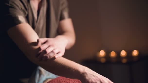 Profesyonel bir fizyoterapist masörünün erkek eli loş ışıklı masaj odasında bayan bir hastaya bel masajı yapıyor. — Stok video