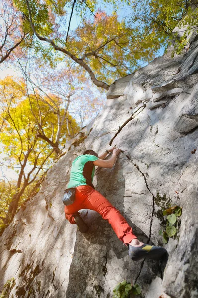 Ein frei gealterter männlicher Kletterer hängt an einer Felswand in einem Wald in den Bergen. Reifes Sportkonzept — Stockfoto