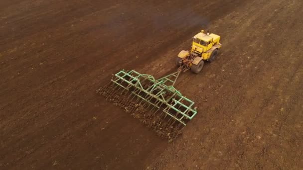 Egy sárga traktor légi rálátása egy pótkocsival, amint szántja a földet művelt területen, mielőtt gabonát ültet. Az a koncepció, hogy előkészítse a földet a vetőmagok talajba ültetésére. Gazdaság — Stock videók