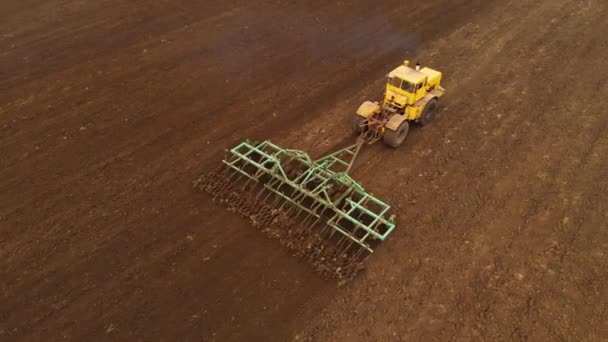 Veduta aerea di un trattore giallo con un rimorchio arare un terreno arare un campo coltivato prima di piantare cereali. Il concetto di preparare il terreno per piantare semi nel terreno. Azienda agricola — Video Stock