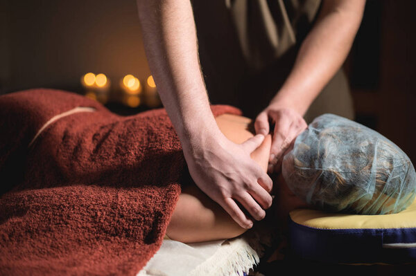 Professional massage of the shoulder and trapezius muscle indoors with cozy dark lighting. Premium massage. Male physiotherapist massage therapist doing upper back massage to a female client