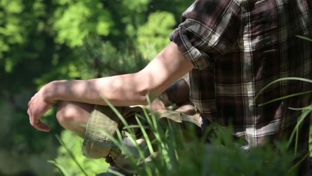 Young man sits in lotus position on top, looks down. Summer, sunny day, closeup — Stock Video