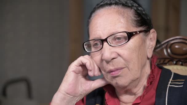 Portrait d'une femme âgée et chérissante portant des lunettes, appuyée sur son bras à l'intérieur, assise et réfléchie. Femme âgée 80 ans — Video