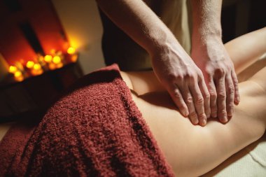 Mens premium kalça masajı anti-selülit sağlık merkezi. Ofisteki kadın müşteriye ayak masajı yapan erkek bir masörün yakın plan fotoğrafı. Arka planda yanan mumların ışığı var.