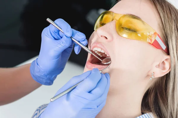 A close-up of the girls face is examined by a dental examiner with his mouth open and a napkin and eyes closed. Dentist hands with inspection tools