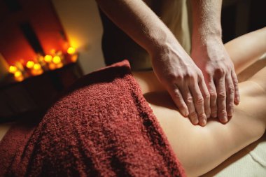Mens premium kalça masajı anti-selülit sağlık merkezi. Ofisteki kadın müşteriye ayak masajı yapan erkek bir masörün yakın plan fotoğrafı. Arka planda yanan mumların ışığı var.