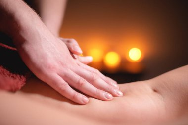 Mens premium kalça masajı anti-selülit sağlık merkezi. Ofisteki kadın müşteriye ayak masajı yapan erkek bir masörün yakın plan fotoğrafı. Arka planda yanan mumların ışığı var.