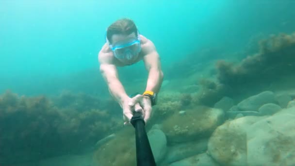 Hombre musculoso con máscara nada bajo el agua, sosteniendo la cámara delante. Primer plano . — Vídeos de Stock