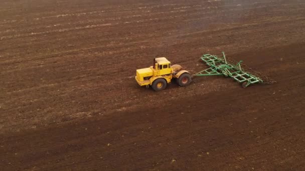 Flygfoto av en gul traktor med en släpvagn som plöjer en mark som plöjs ett odlat fält innan spannmål planteras. Begreppet att förbereda marken för sådd av frön i jorden. Jordbruk — Stockvideo