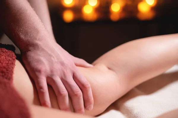 Mens premium luxe heupmassage anti-cellulitis wellnesscentrum. Close-up van een mannelijke masseur doen been massage aan een vrouwelijke klant in een kantoor met donker licht op een achtergrond van brandende kaarsen — Stockfoto