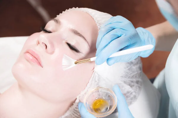 Garota esteticista aplica uma escova para rejuvenescer uma máscara no rosto de uma menina atraente em um salão de spa. O conceito de autocuidado e rejuvenescimento — Fotografia de Stock