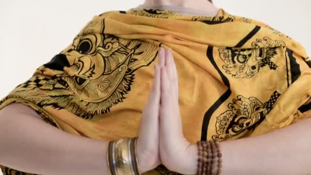 Ένα κορίτσι με ράμες και χέρια με βραχιόλια σε μια χειρονομία ναμαστά και Namaskar. Το κορίτσι σε ένα αυθεντικό κασκόλ εξάσκηση διαλογισμού στέκεται στο στούντιο σε λευκό φόντο — Αρχείο Βίντεο