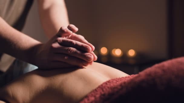 Gros plan Un jeune massothérapeute fait un massage du dos à une femme tatouée dans une salle de massage avec des lumières tamisées sur le fond des bougies. Concept de massage premium low key — Video