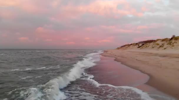 Повітряний вигляд безпілотних літальних апаратів низький політ над пустельним пляжем на заході сонця. Піщаний берег з прокатними хвилями і рожевими хмарами над горизонтом. Морський пейзаж — стокове відео