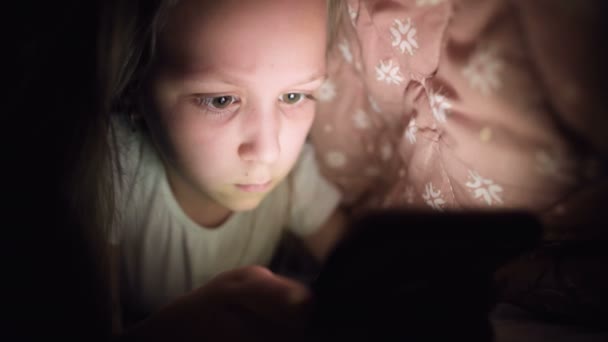 Küçük bir kız uyuduktan sonra dijital tablet akıllı telefon cihazı kullanmak için battaniyenin altına saklanıyor. Küçük çocukların yalnızlığı ve telefonda kurtarma.. — Stok video