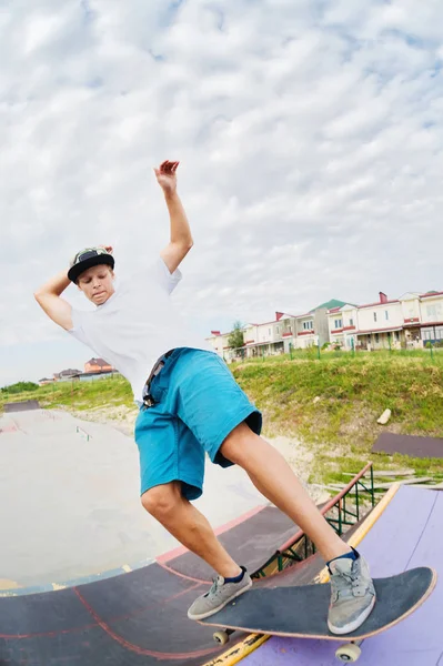 Retrato de un patinador joven haciendo un truco en su monopatín en una rampa de media pipa en un parque de skate en el verano en un día soleado. El concepto de cultura juvenil del ocio y el deporte — Foto de Stock