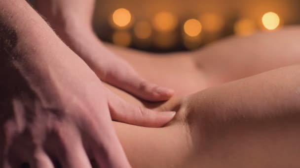 Close-up de massagem premium anti-celulite na coxa. As mãos masculinas fazem a massagem de bem-estar da coxa à menina paciente em um estudo acolhedor com a luz escura. Serviços de massagens de luxo — Vídeo de Stock